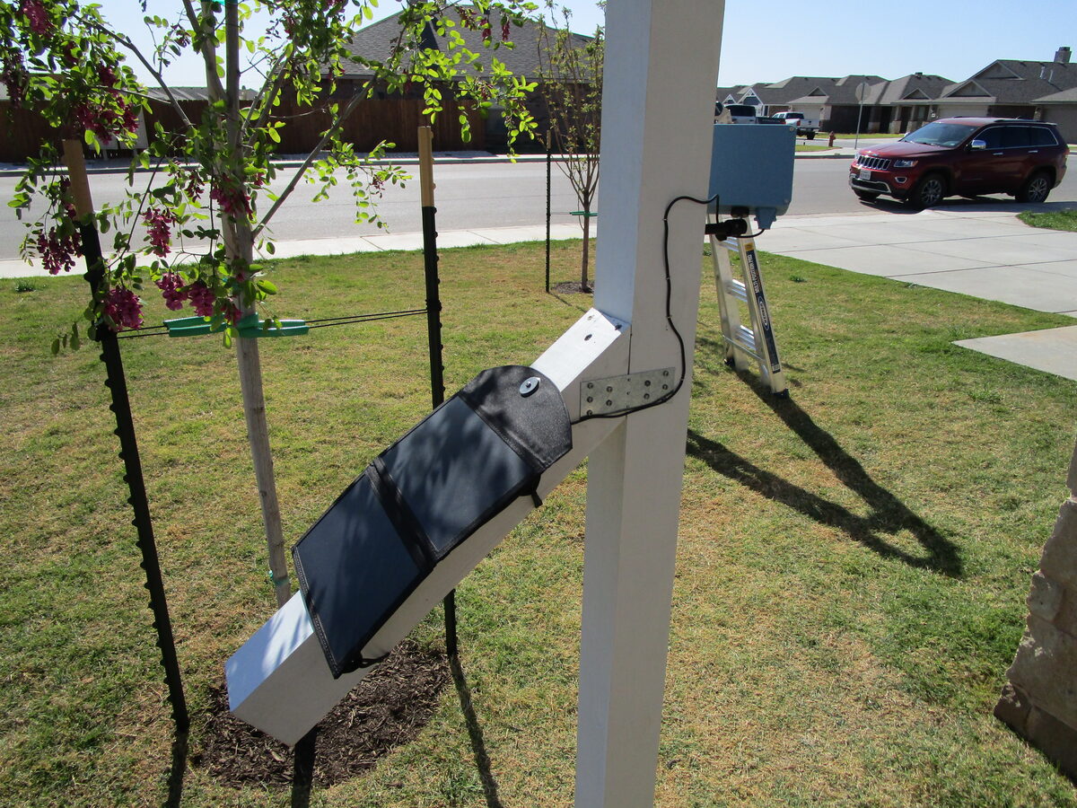 Close-up of the angled solar panel mounted to the birdhouse post, with the weatherproof Pi enclosure above it