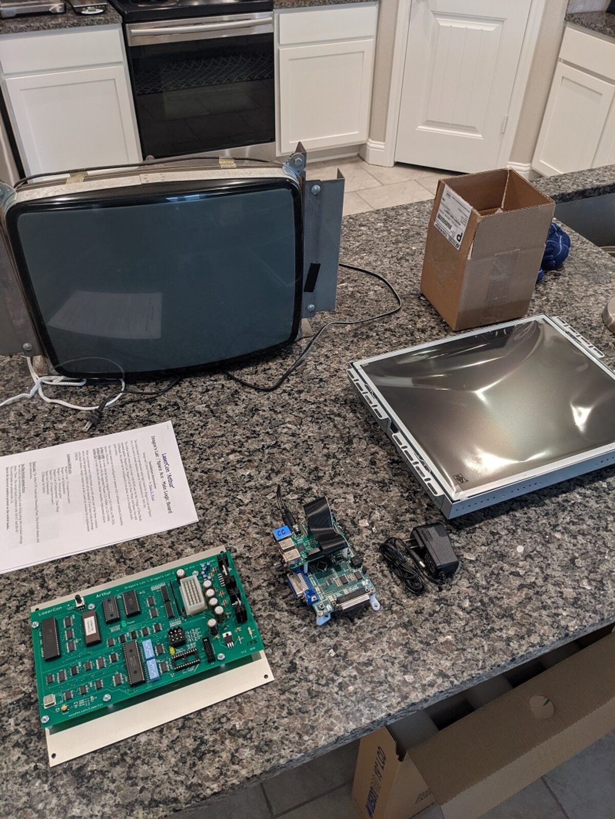 New replacement boards, a Raspberry Pi, and a flat LCD panel laid out on a kitchen counter next to the old CRT being removed